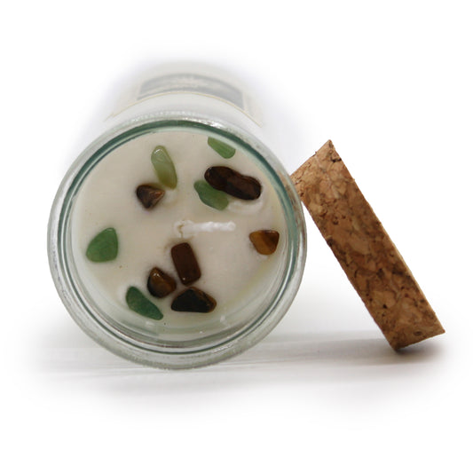 Candle in a glass jar with decorative stones and a cork lid on a white background