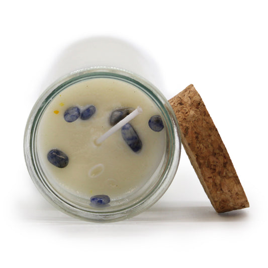 Candle in a glass jar with decorative stones and a cork lid on a white background