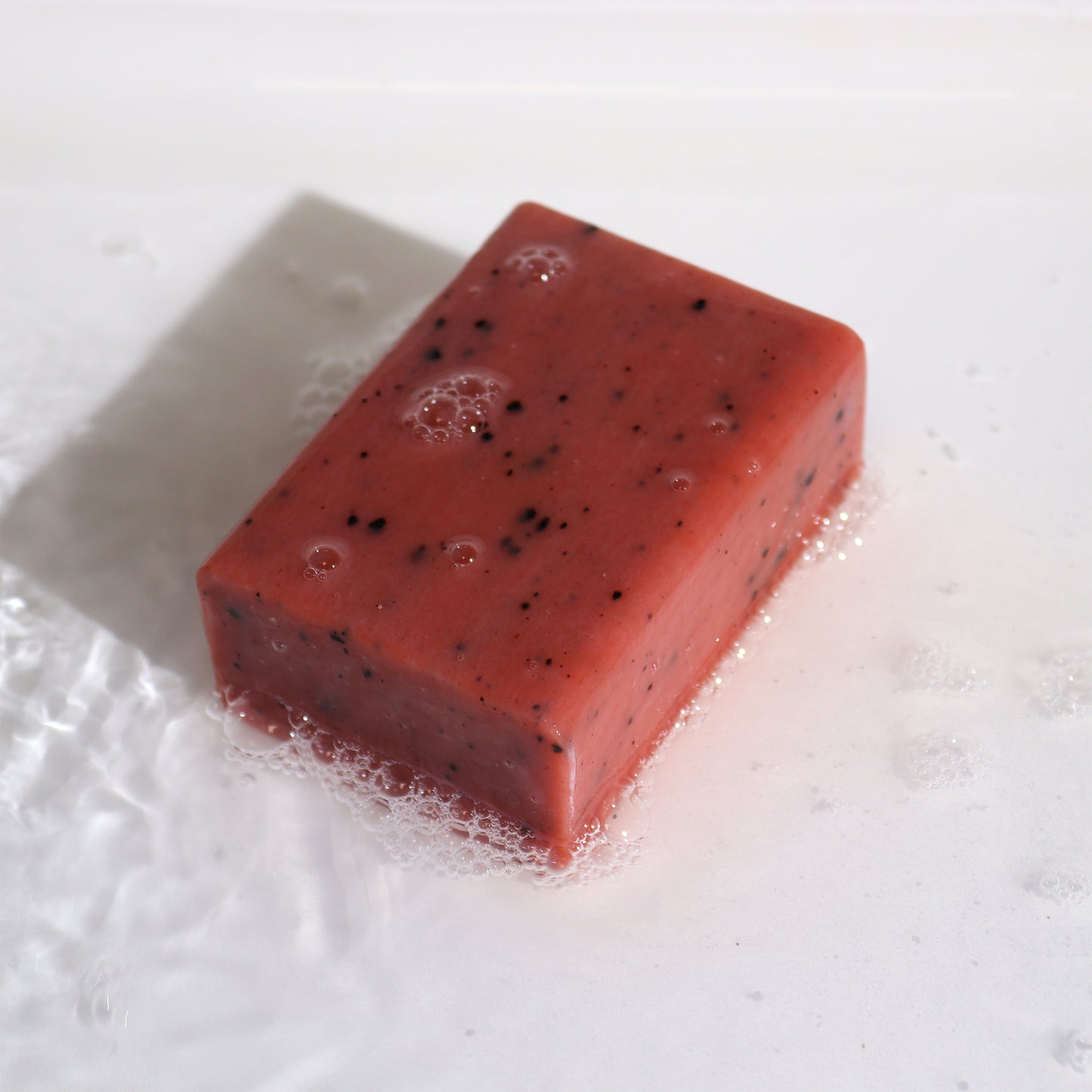 Red soap bar with black specks on a white background and soap bubbles