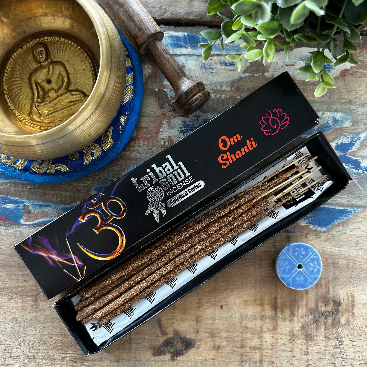 Box of Tribal Soul Incense Om Shanti with incense sticks on a wooden surface with a plant and other items.