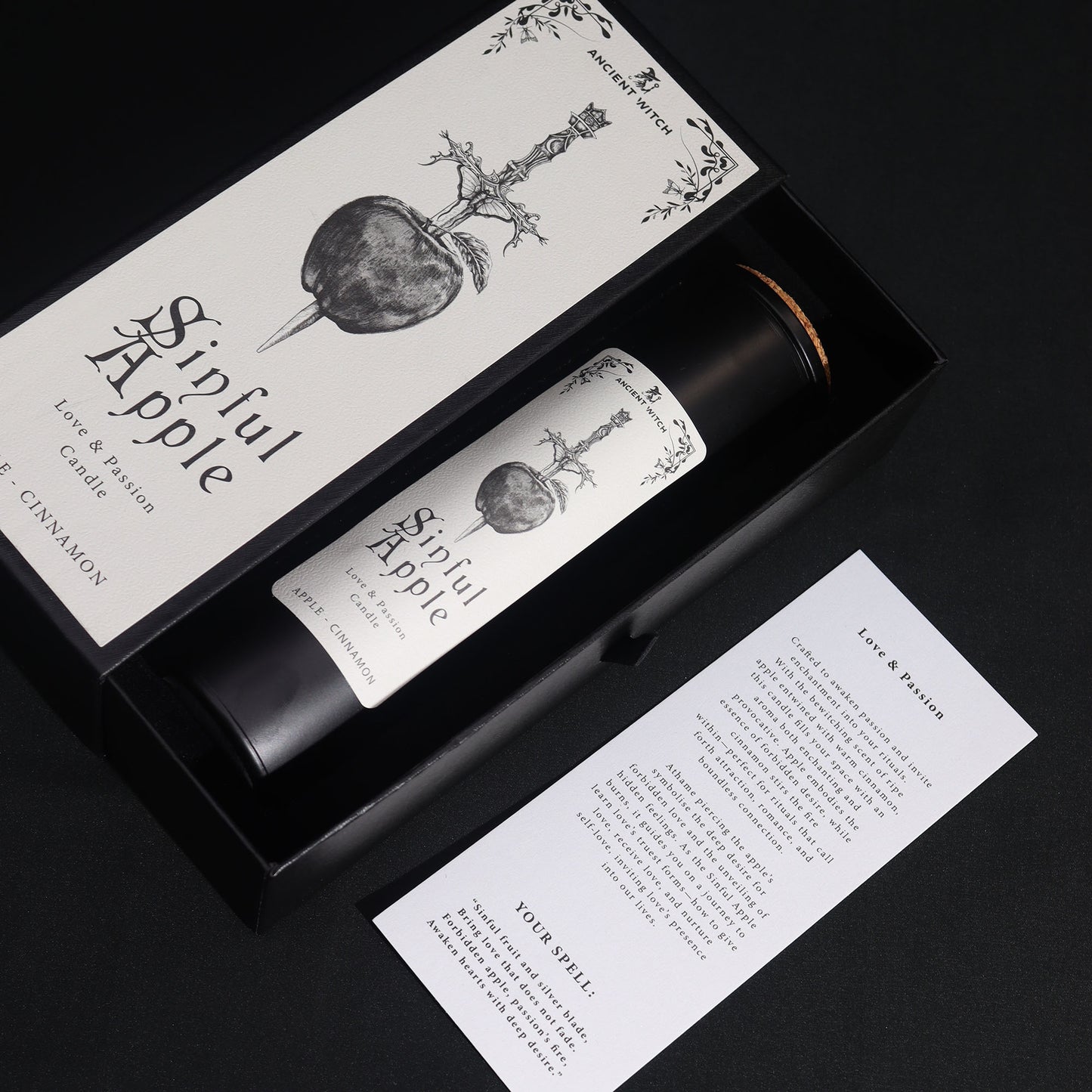 angle view Sinned Apple candle in packaging with label and information sheet on a black background