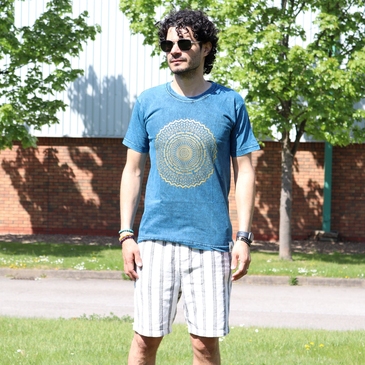 Man wearing black sun glasses a blue t-shirt with a yellow design outdoors
