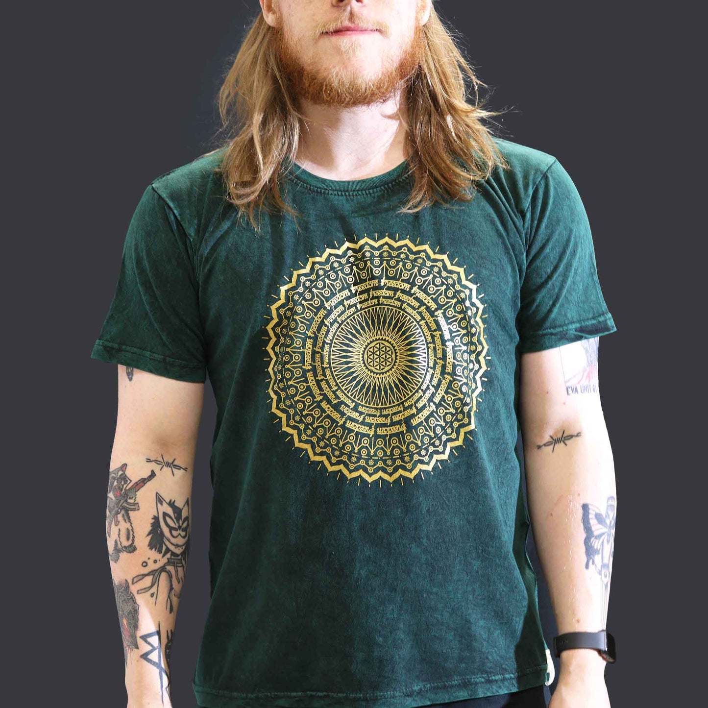 Person wearing a green t-shirt with a gold mandala design on a dark background
