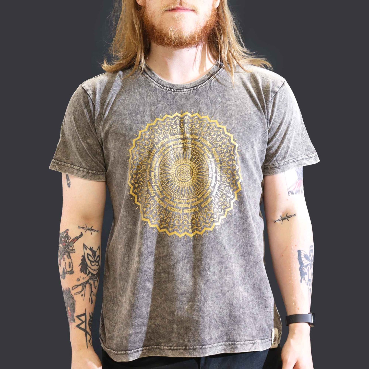 Person wearing a gray t-shirt with a gold mandala design on a dark background
