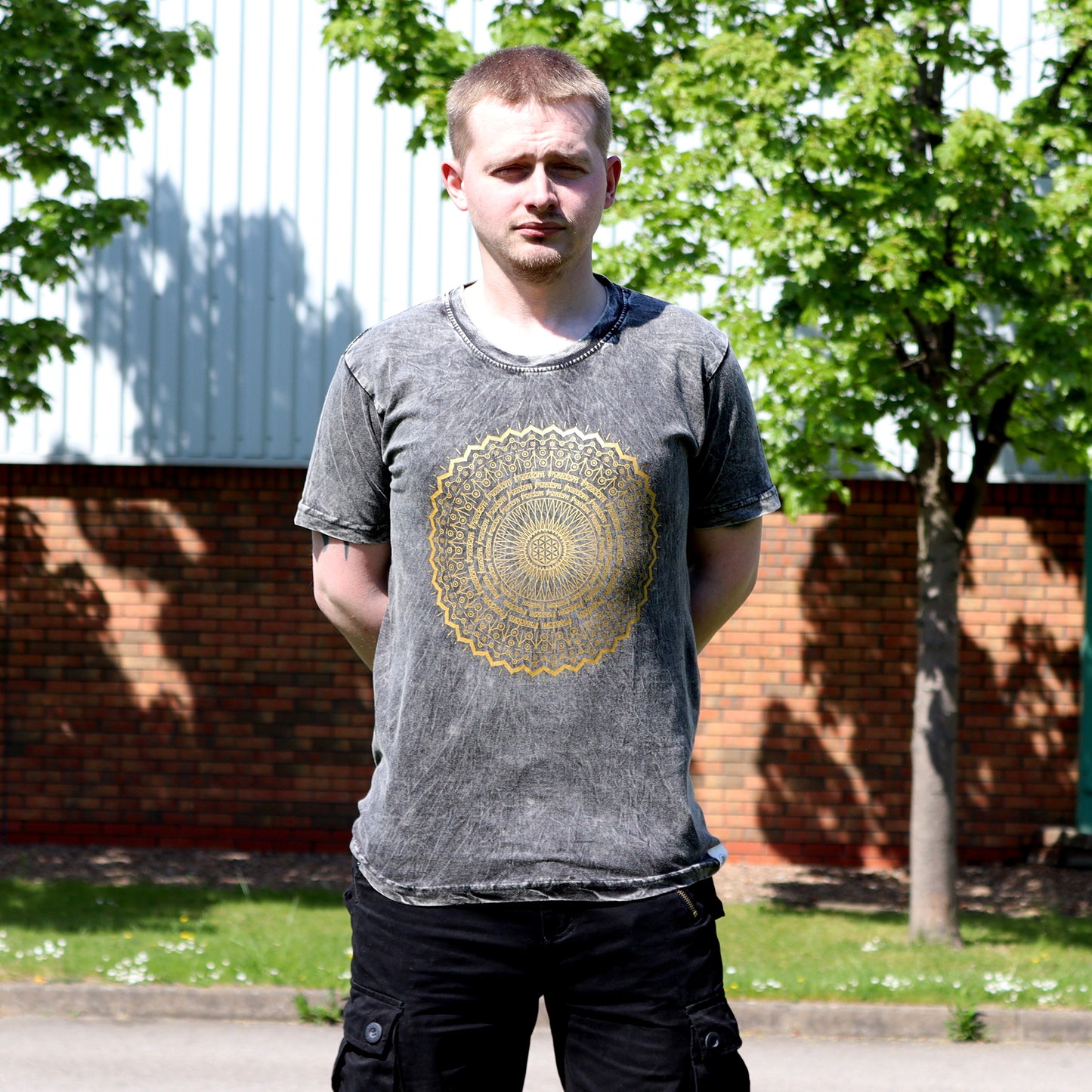 Man wearing a gray t-shirt with a gold circular design outdoors.
