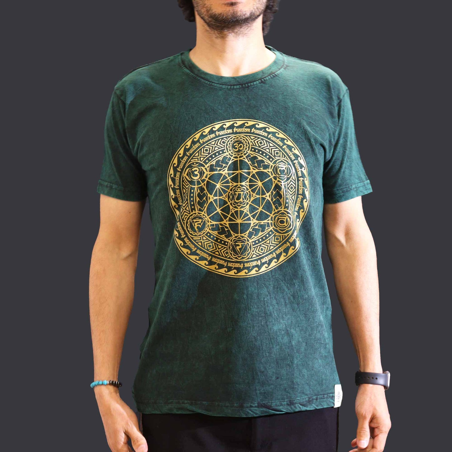 front view of Person with a black beard wearing a green t-shirt with a gold geometric Chakra design on a dark background