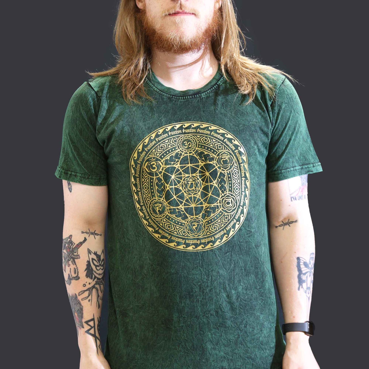 Person with ginger hair wearing a green t-shirt with a gold circular Chakra design on a plain background