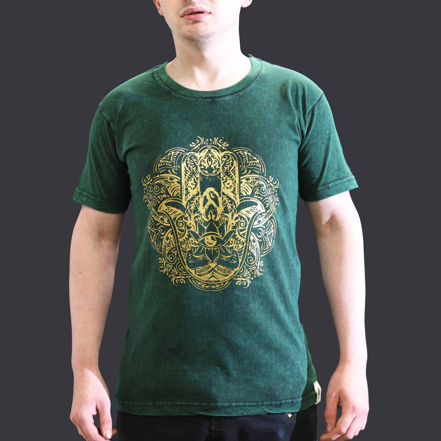 Person wearing a green t-shirt with a gold intricate design on a dark background
