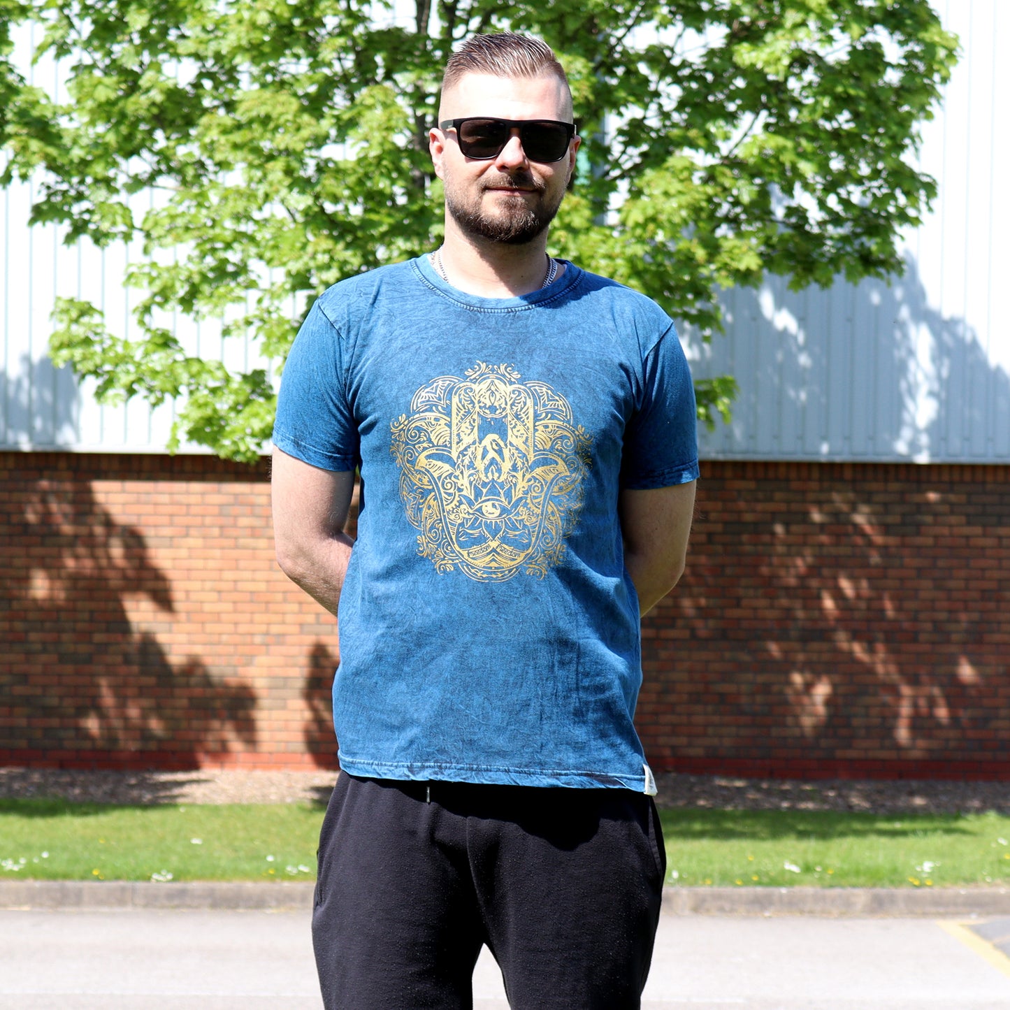Man wearing a blue t-shirt with a gold Hamsa design standing outdoors