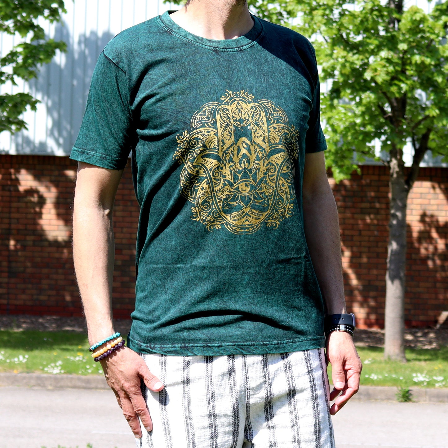 Person wearing a green t-shirt with a gold hamsa graphic design outdoors.