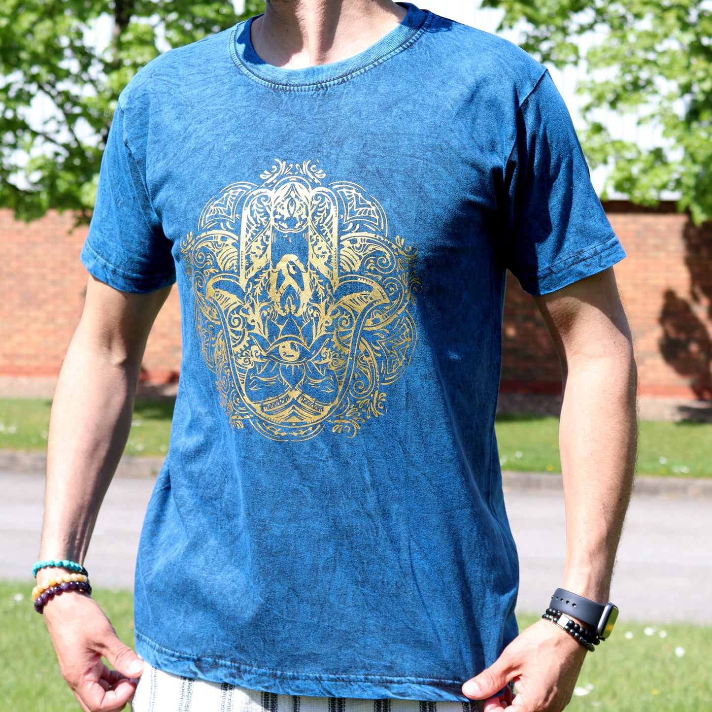 Person wearing a blue t-shirt with a yellow Hamsa design outdoors.