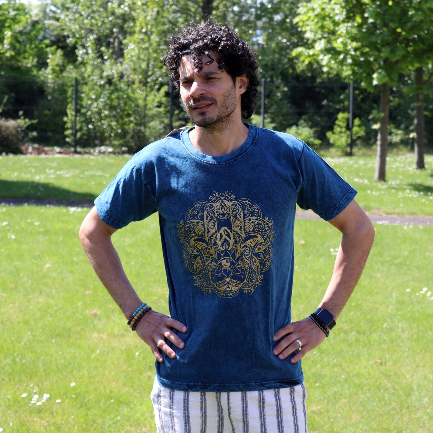 Man wearing a blue t-shirt with a gold hamsa design in a park