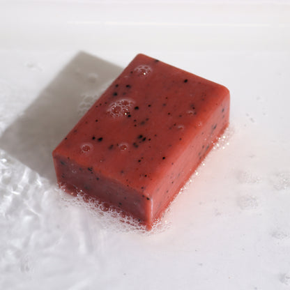Red soap bar with black specks on a white background and soap bubbles
