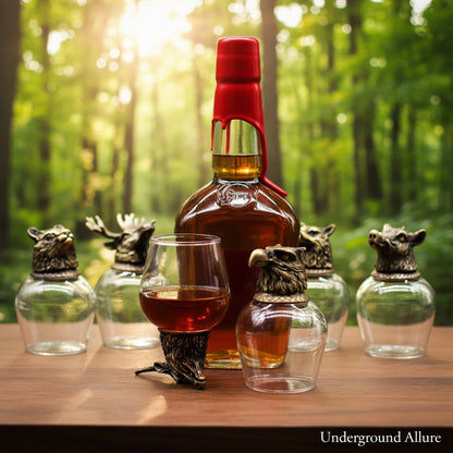 Bottle of whiskey with a red cap and Wild Forest Creatures 100ml glasses on a wooden table in a forest setting, featuring the brand 'Underground Allure