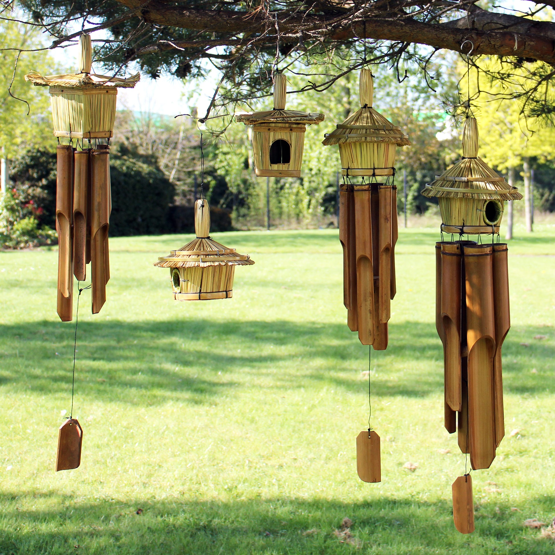 Set of bamboo birdhouses and wind chimes hanging from a tree in a garden.