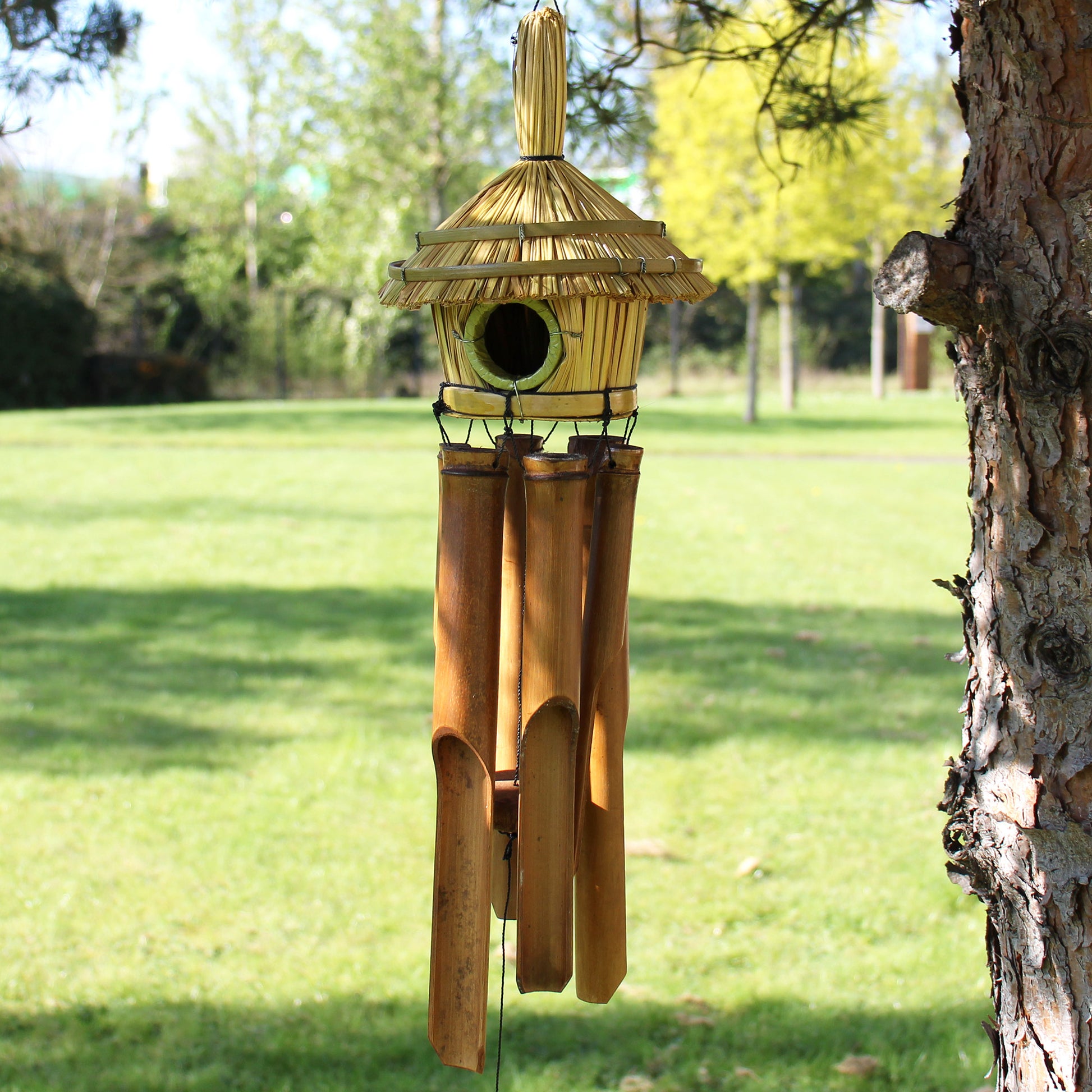 Bamboo birdhouse with wind chime attached to a tree in a garden setting