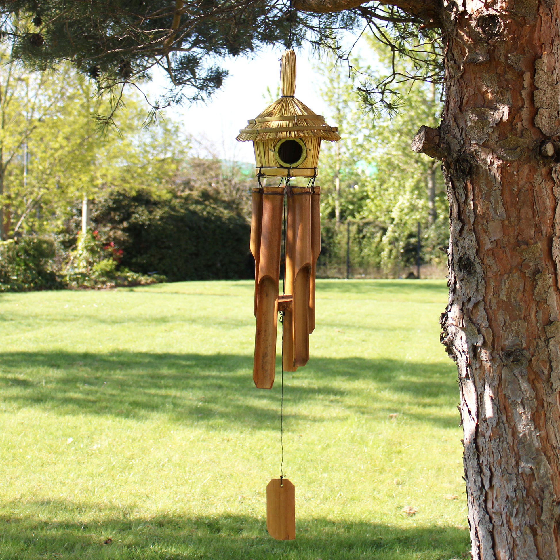 Wooden Birdhouse & wind chime hanging from a tree in a garden setting