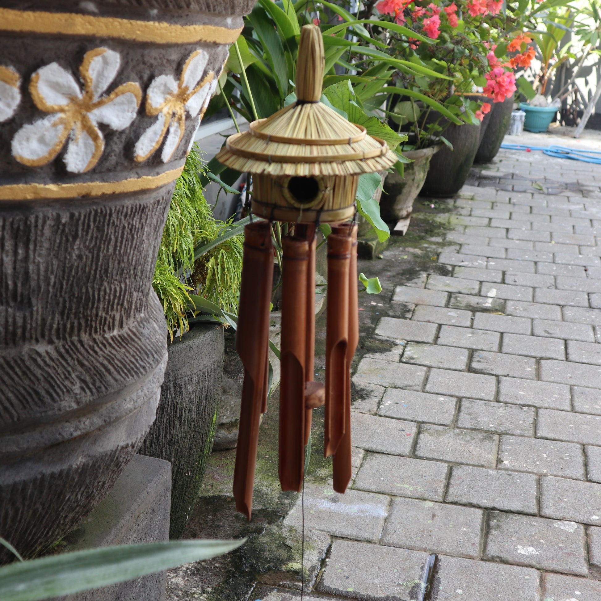 Bamboo wind chime next to a textured pot with floral patterns on a garden path.