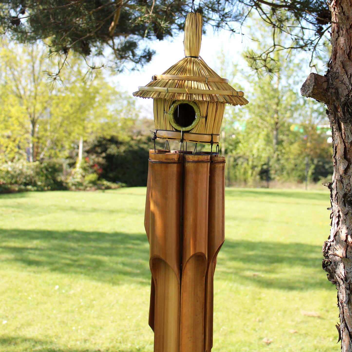 Decorative bamboo birdhouse with thatched roof in a garden setting