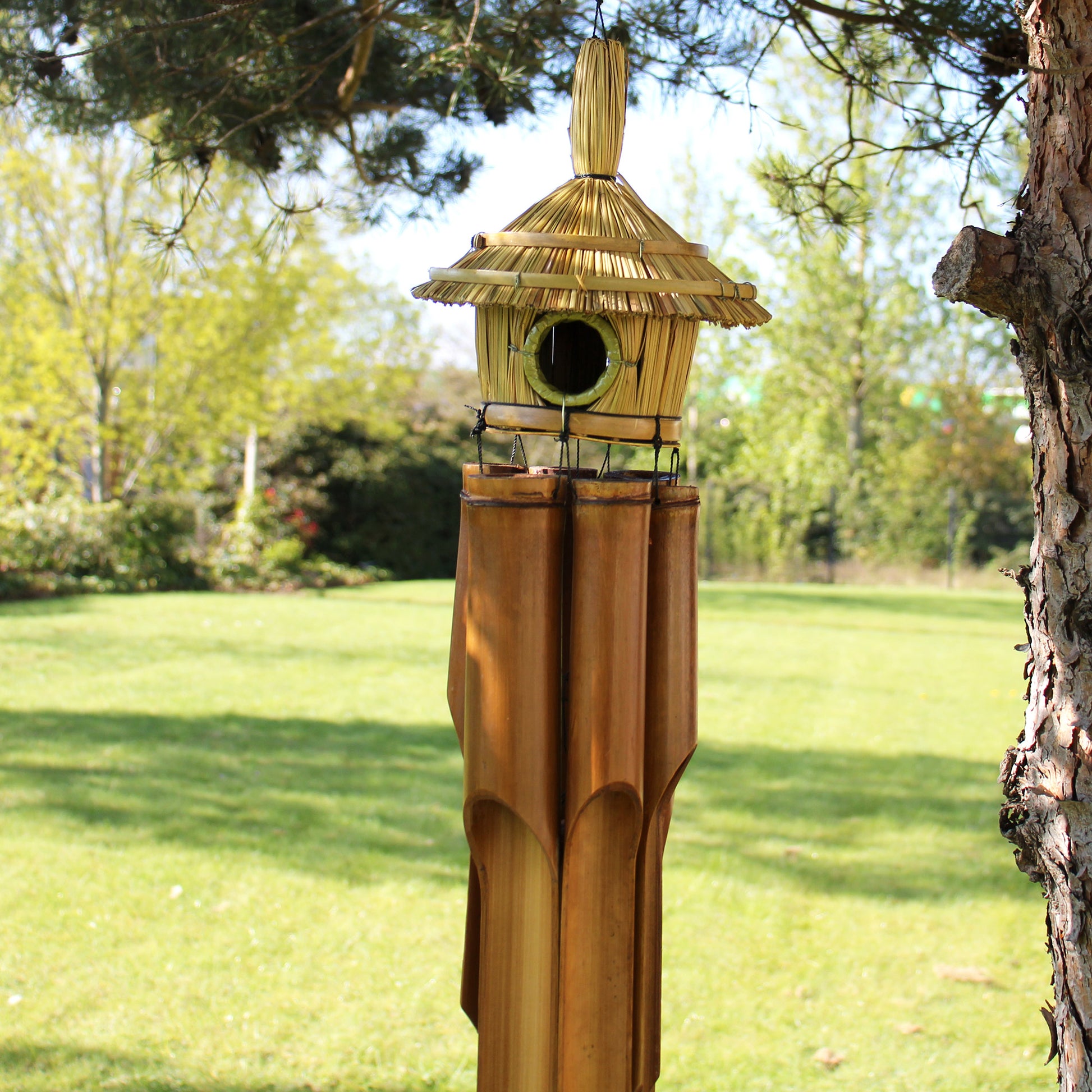 Decorative bamboo birdhouse with thatched roof in a garden setting