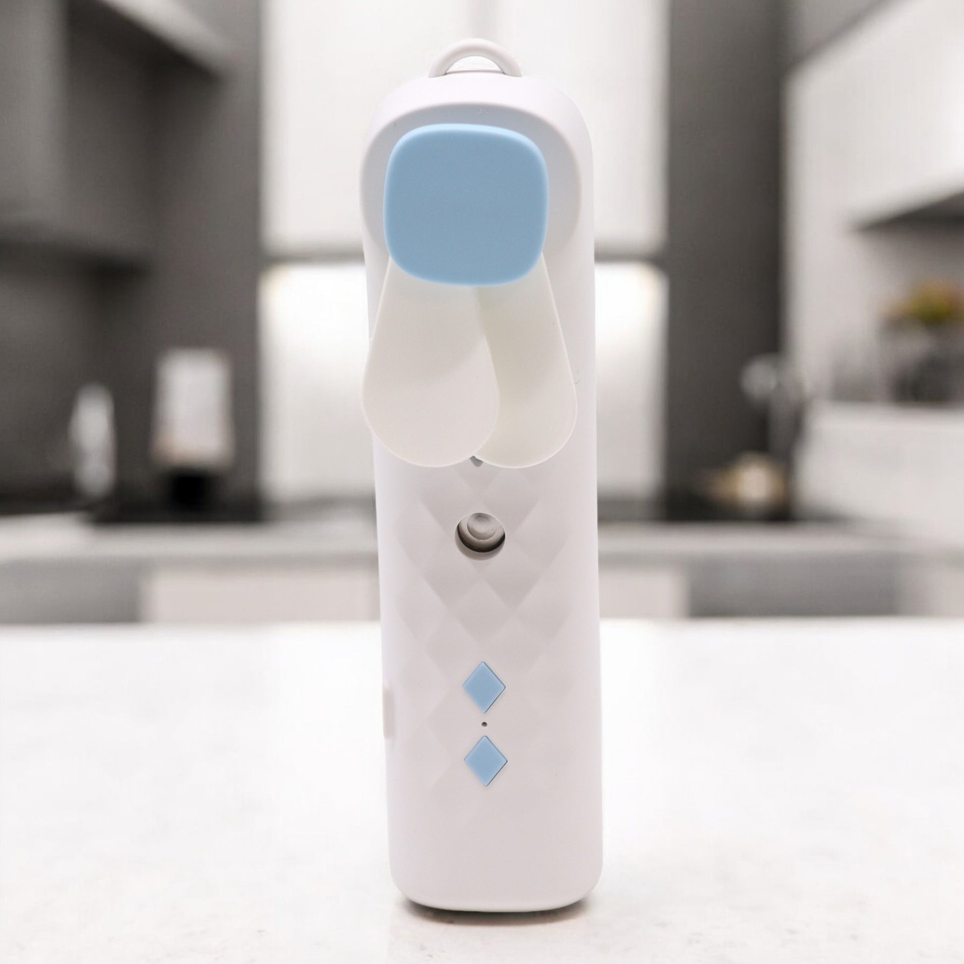 White and blue electric Mist face fan on a white surface with a blurred kitchen background