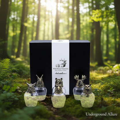 Four glass animal figurines in front of a black box with 'Wild Forest Creatures' branding in a forest setting.