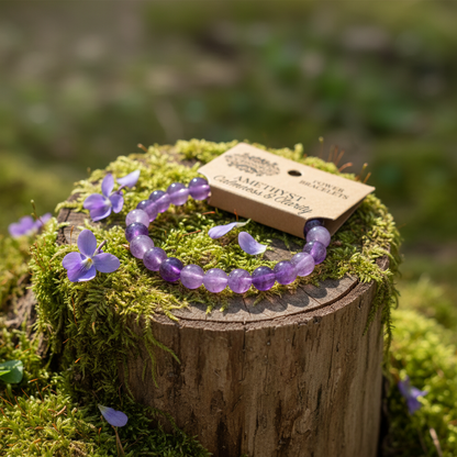 Purple beaded bracelet on a wooden stump with a tag, surrounded by small purple flowers.