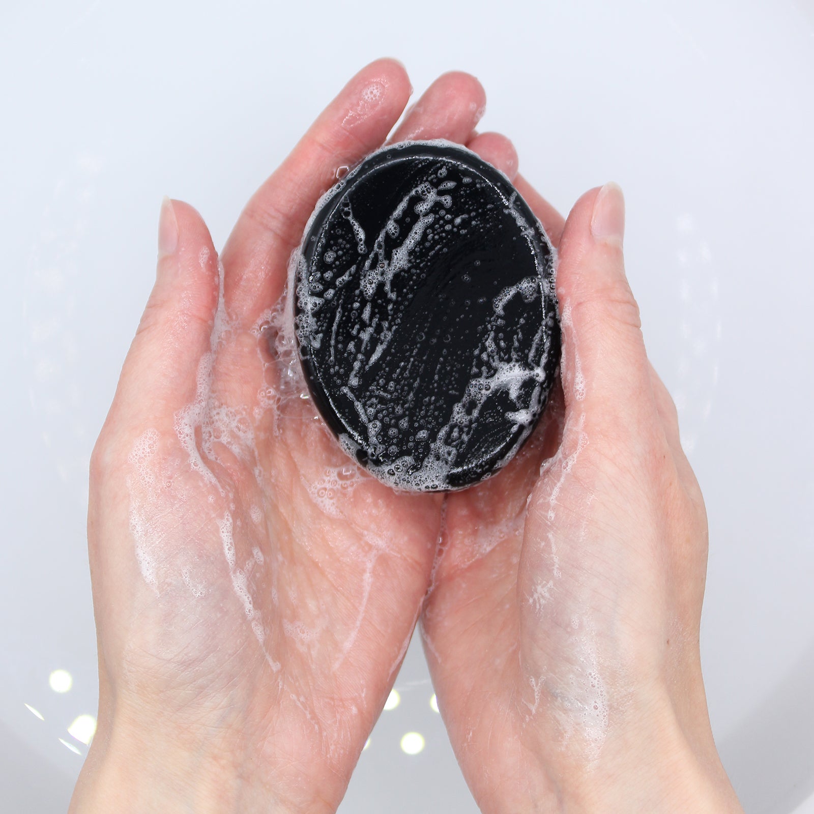 Black exfoliating pad with soap suds held between two hands against a light background