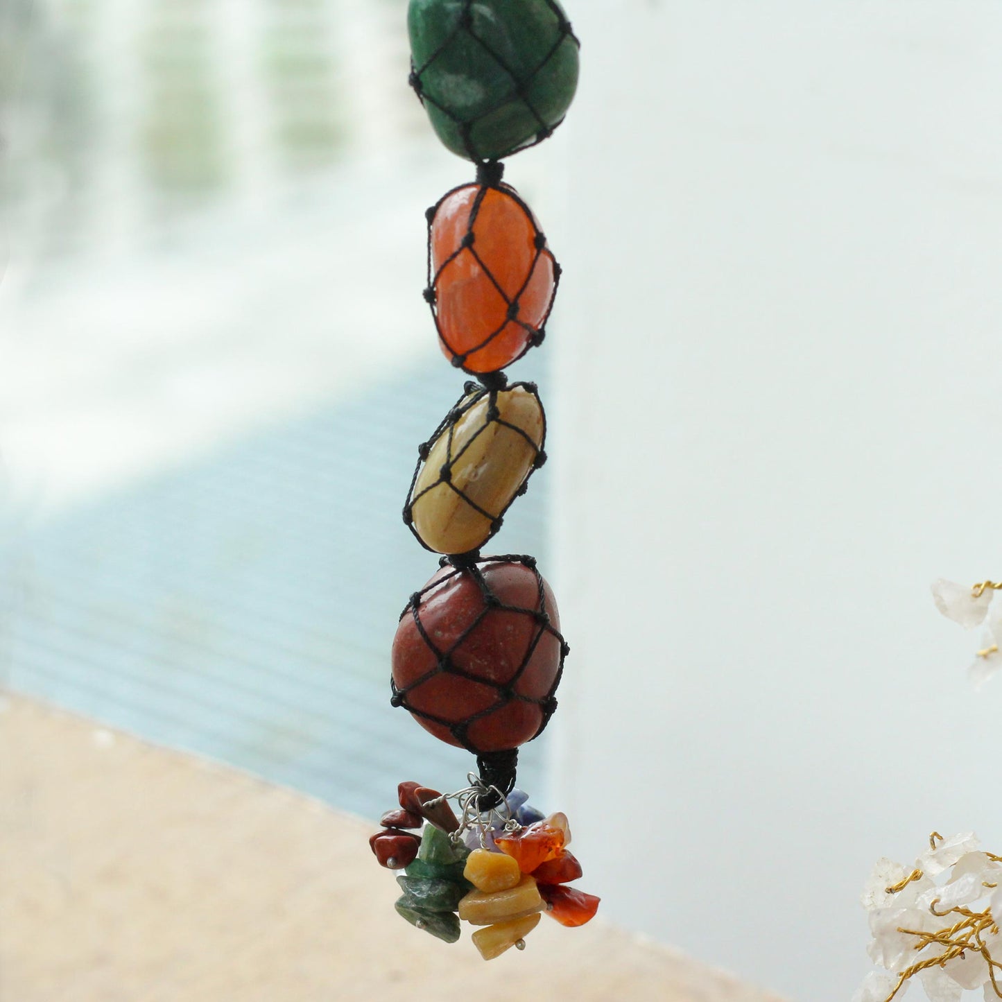 Close up view Hanging Chakra Stone Pendant - Seven Chakra Chips on a blurred beach background