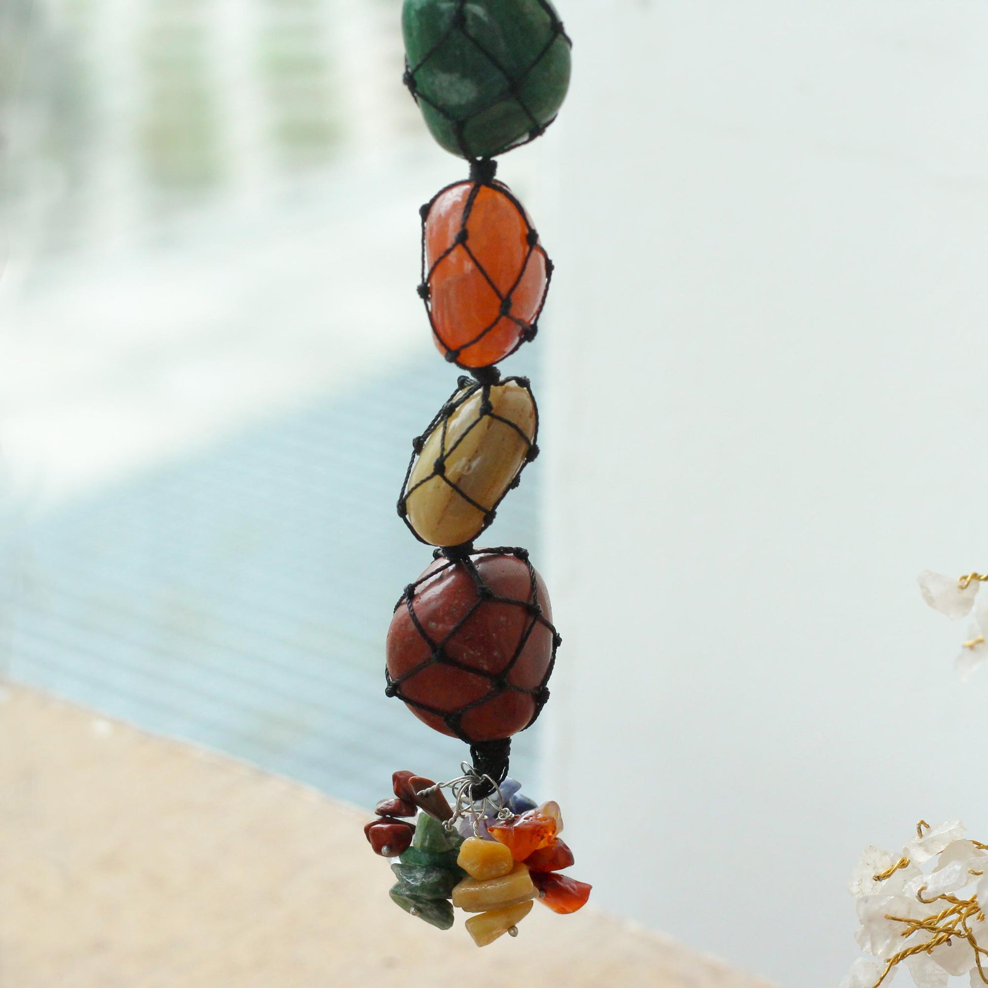 Close up view Hanging Chakra Stone Pendant - Seven Chakra Chips on a blurred beach background