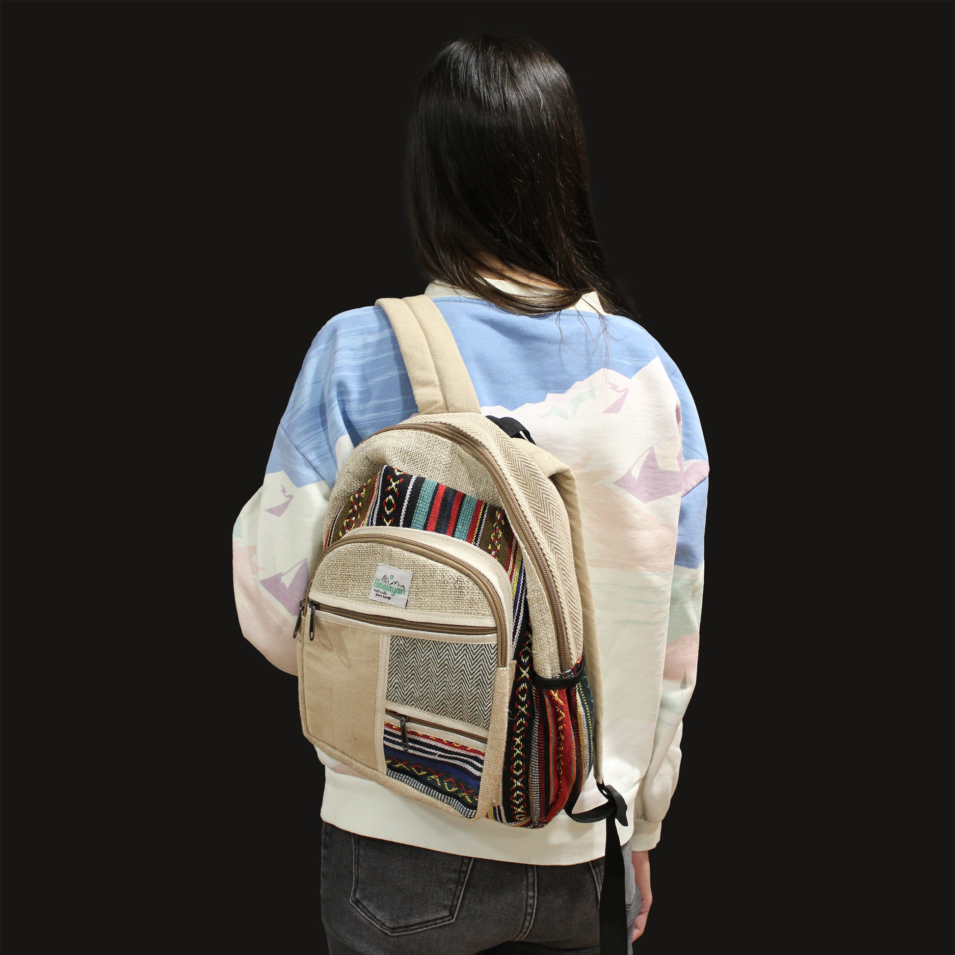 Person wearing a beige backpack with colorful patterns on a black background