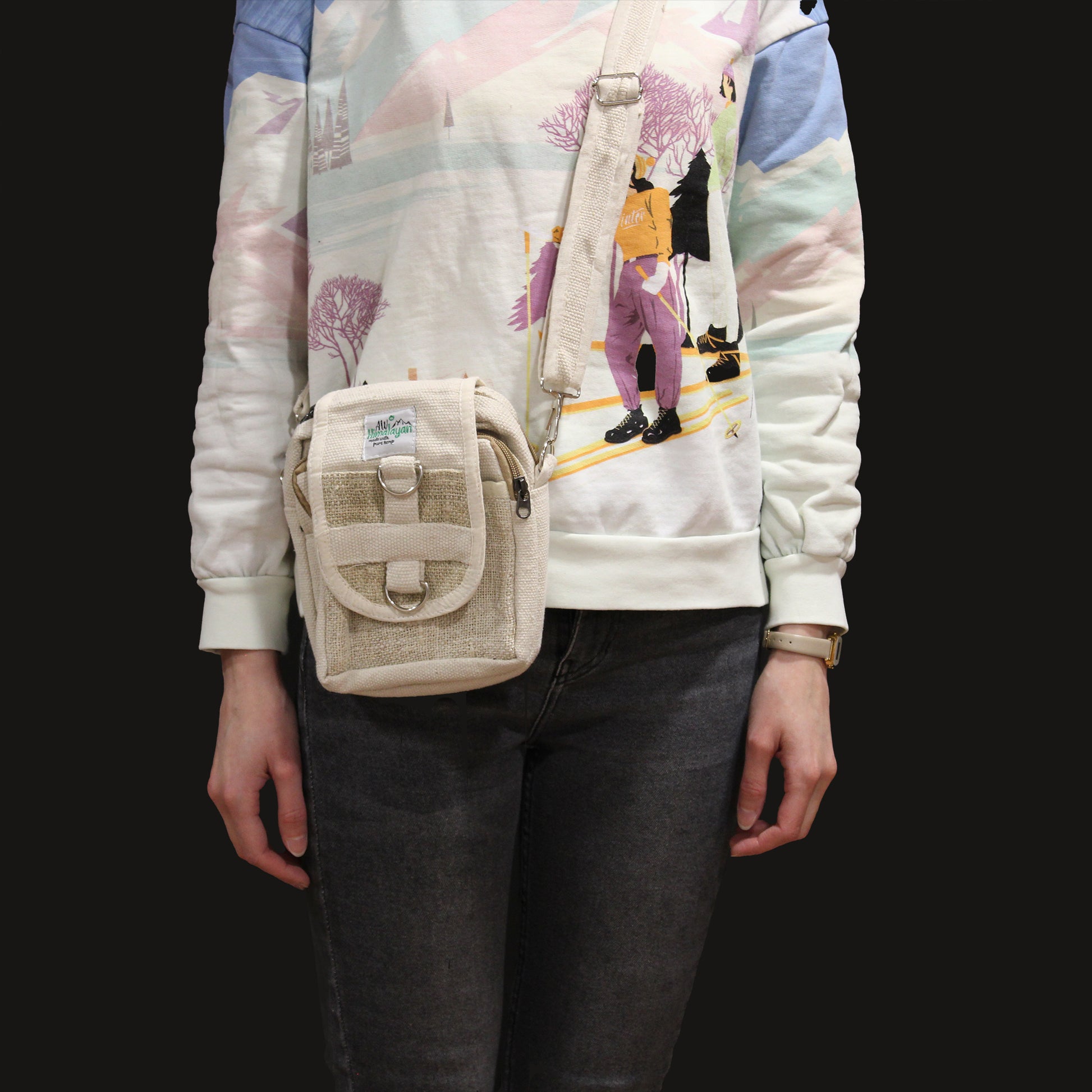 Person wearing a beige crossbody bag with a colorful jacket and dark jeans on a black background