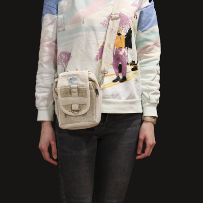 Person wearing a beige crossbody bag with a colorful jacket and dark jeans on a black background