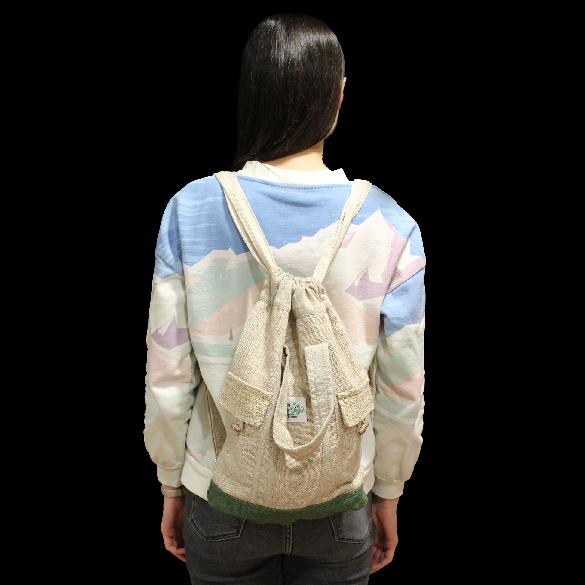 Person wearing a beige drawstring backpack with a colorful shirt on a black background