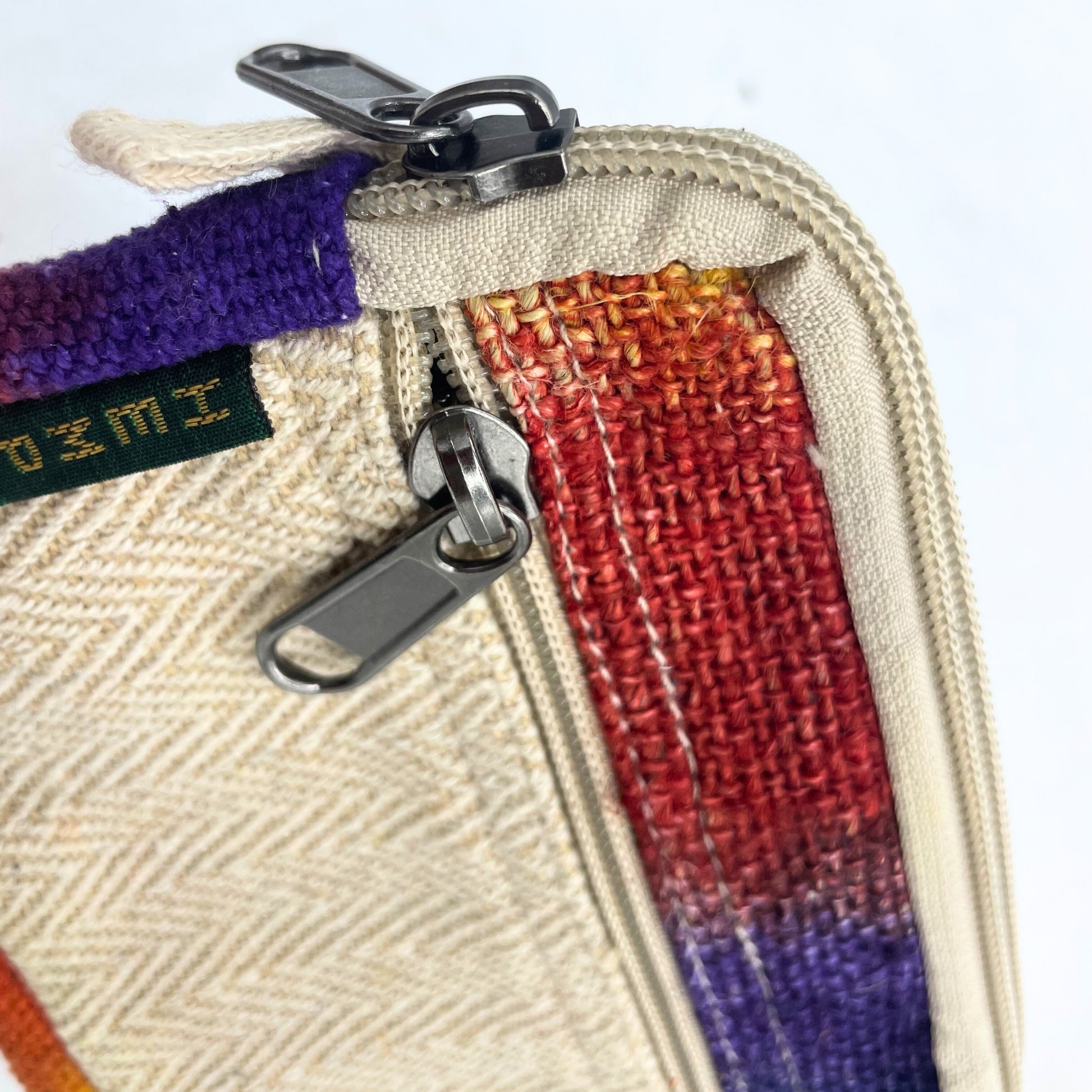 Close-up of a woven pouch with a zipper, featuring a colorful strap and a brand label.