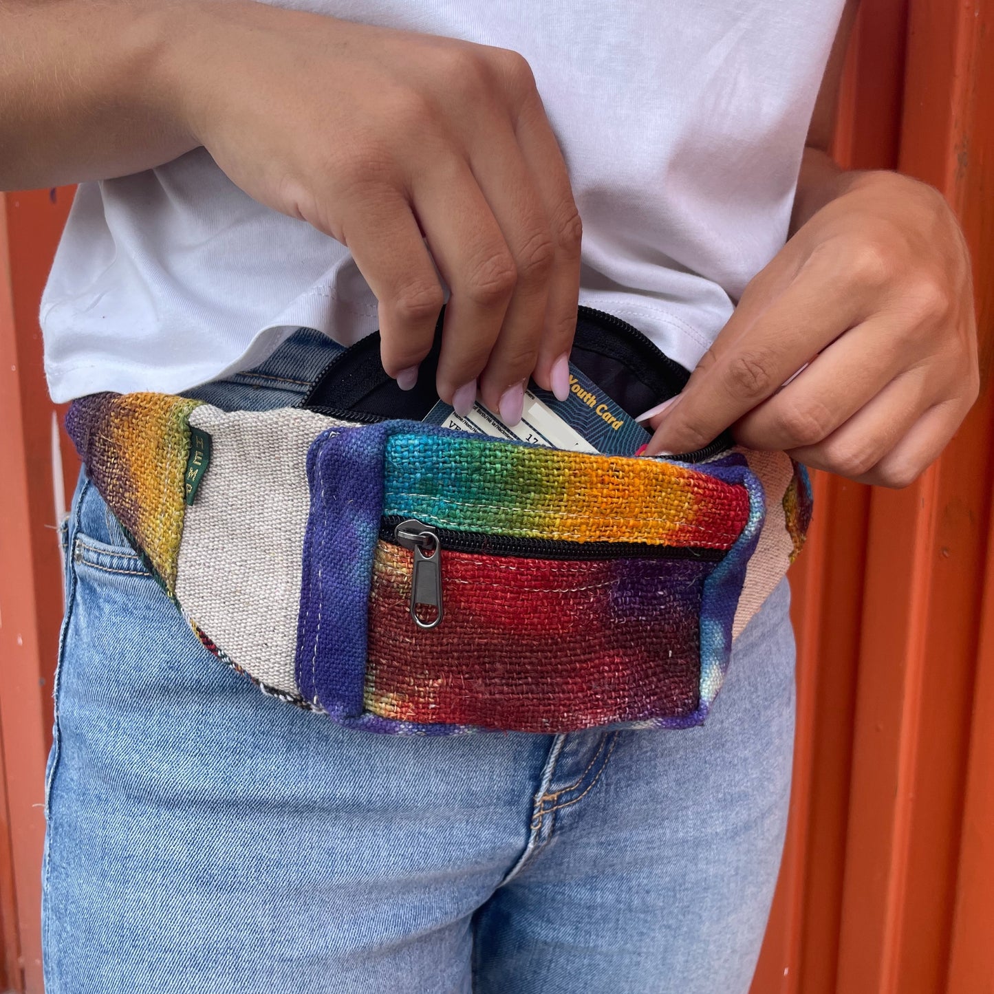 Person wearing a colorful waist bag with money sticking out, against an orange background