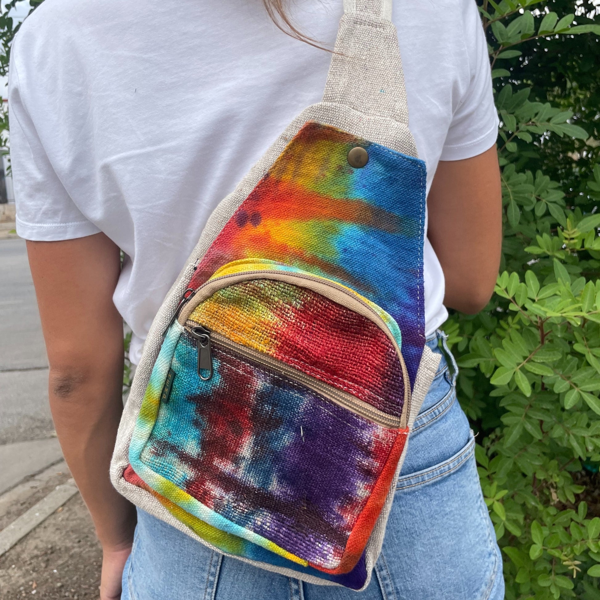 Person wearing a colorful tie-dye sling bag with a white shirt and blue jeans.
