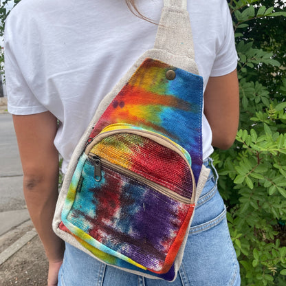 Person wearing a colorful tie-dye sling bag with a white shirt and blue jeans.