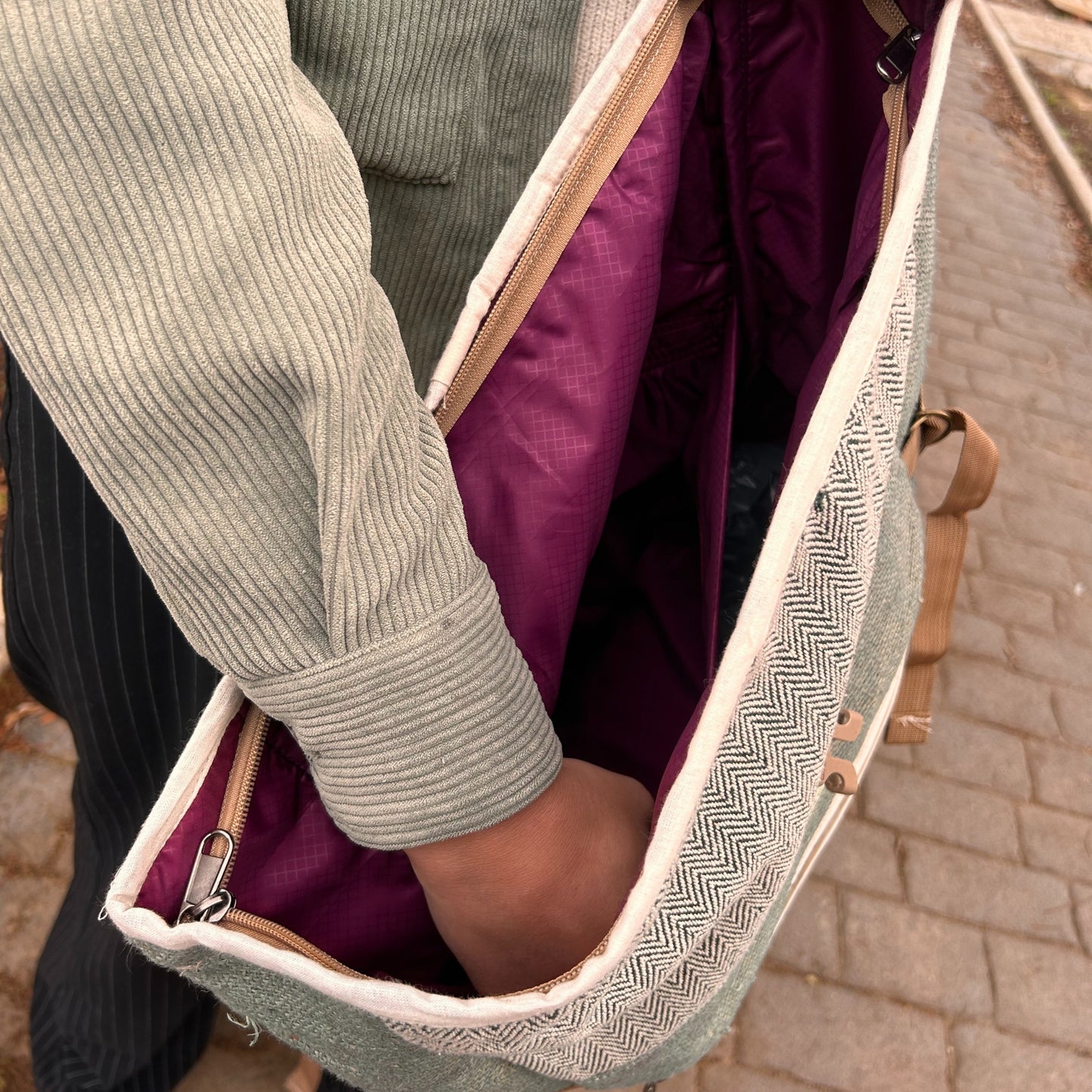 Person holding a green backpack with a purple interior on a paved path.