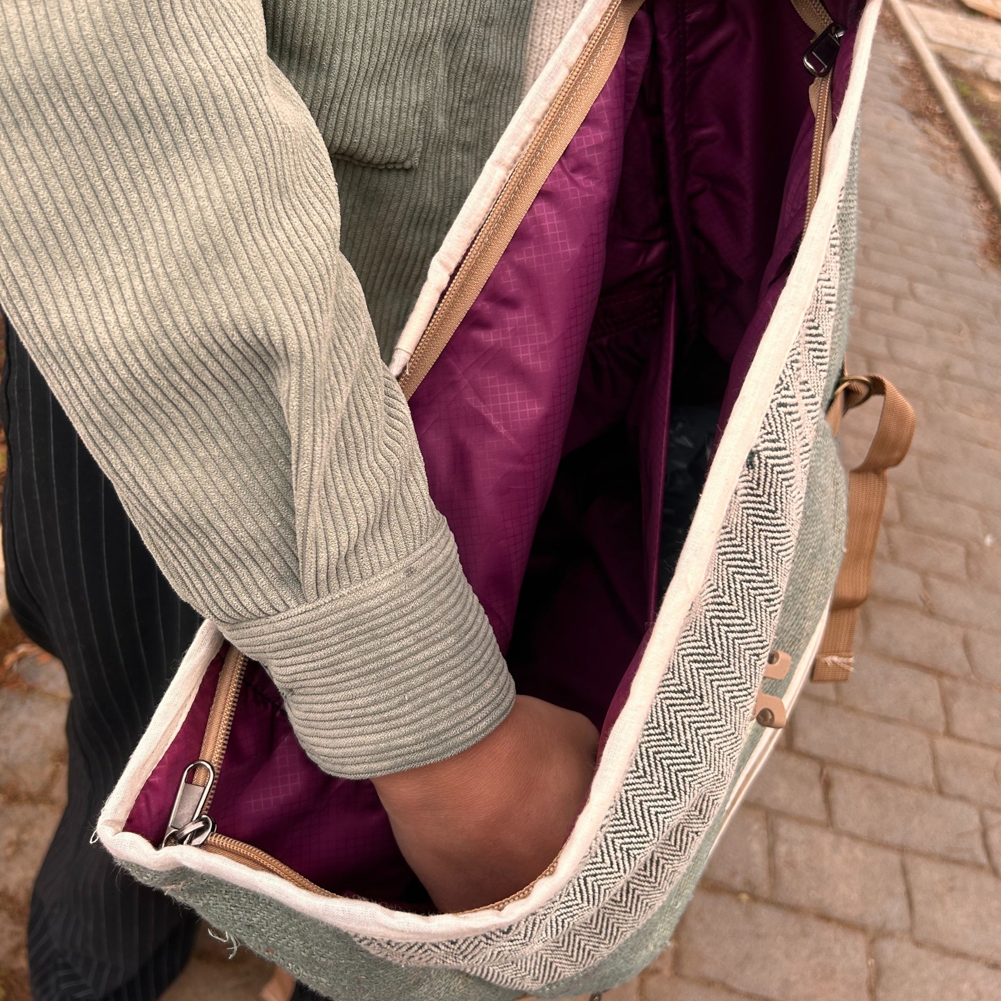 Person holding a green backpack with a purple interior on a paved path.