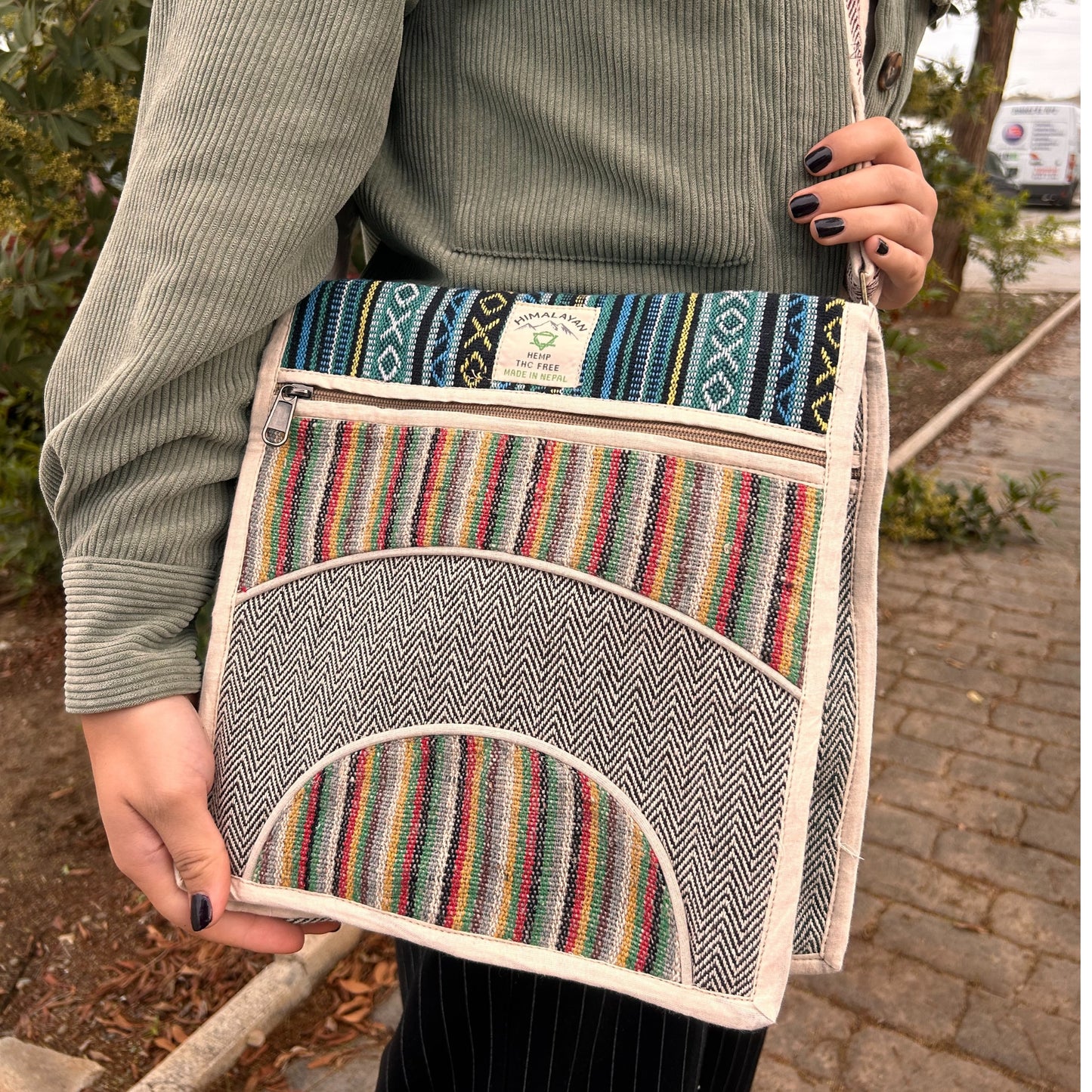 Person holding a colorful striped bag with a brand label outdoors.