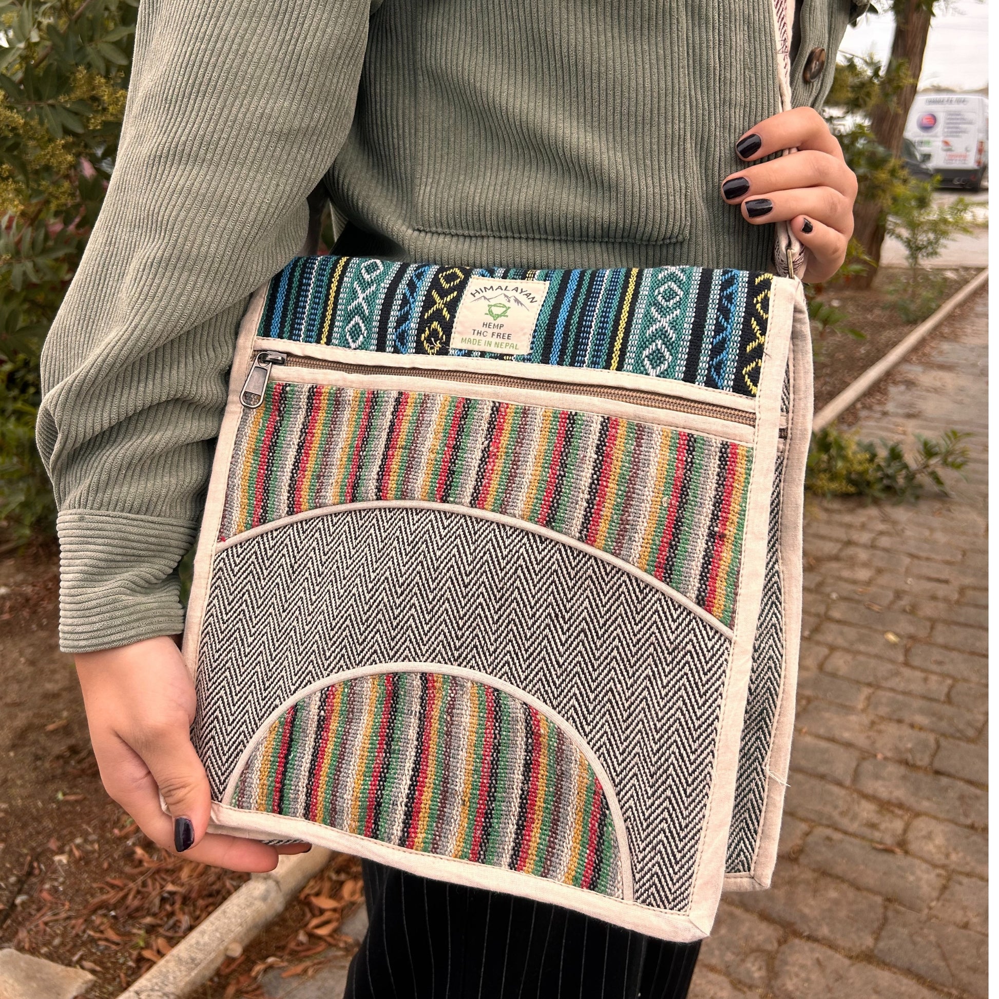 Person holding a colorful striped bag with a brand label outdoors.