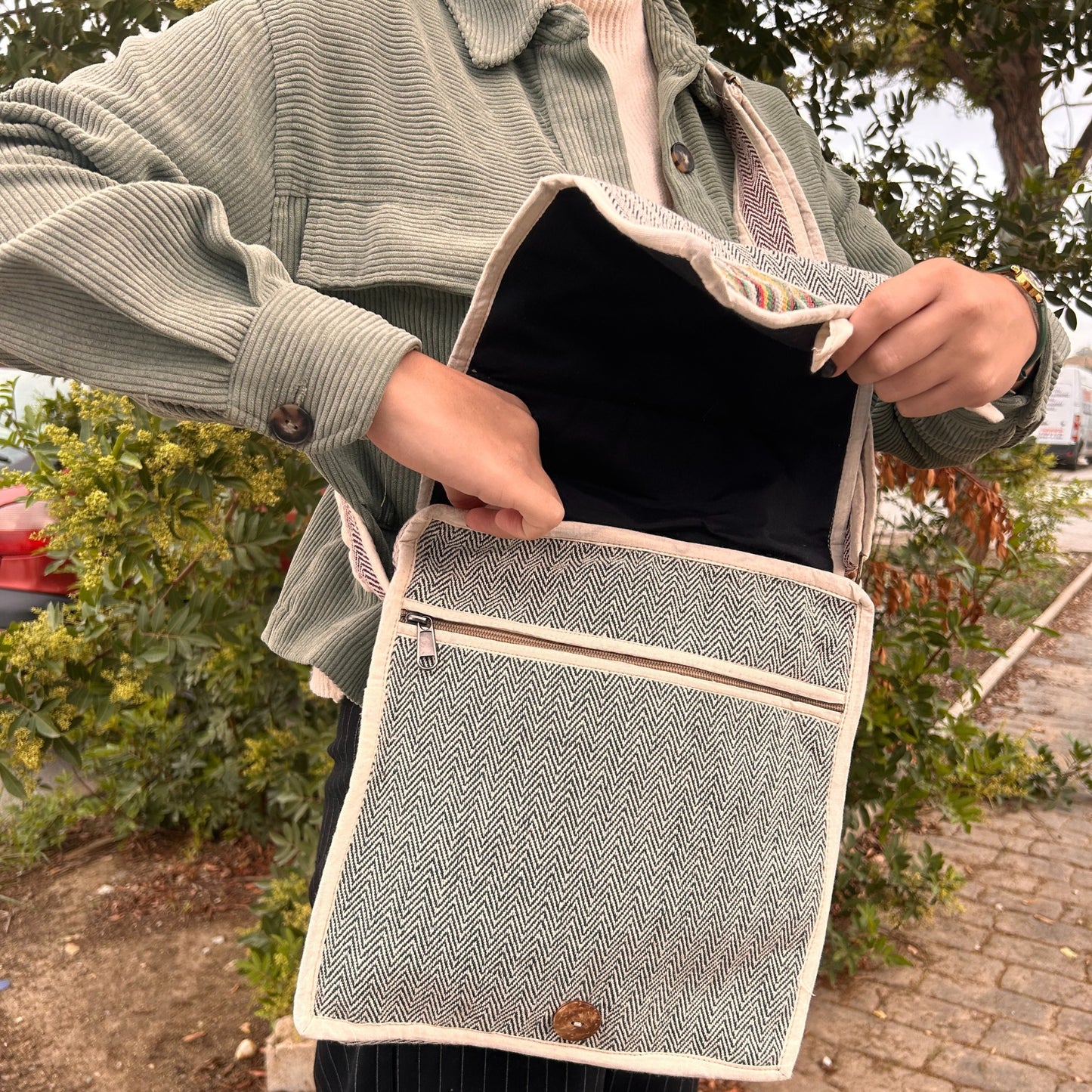 Person holding a patterned bag outdoors with greenery in the background