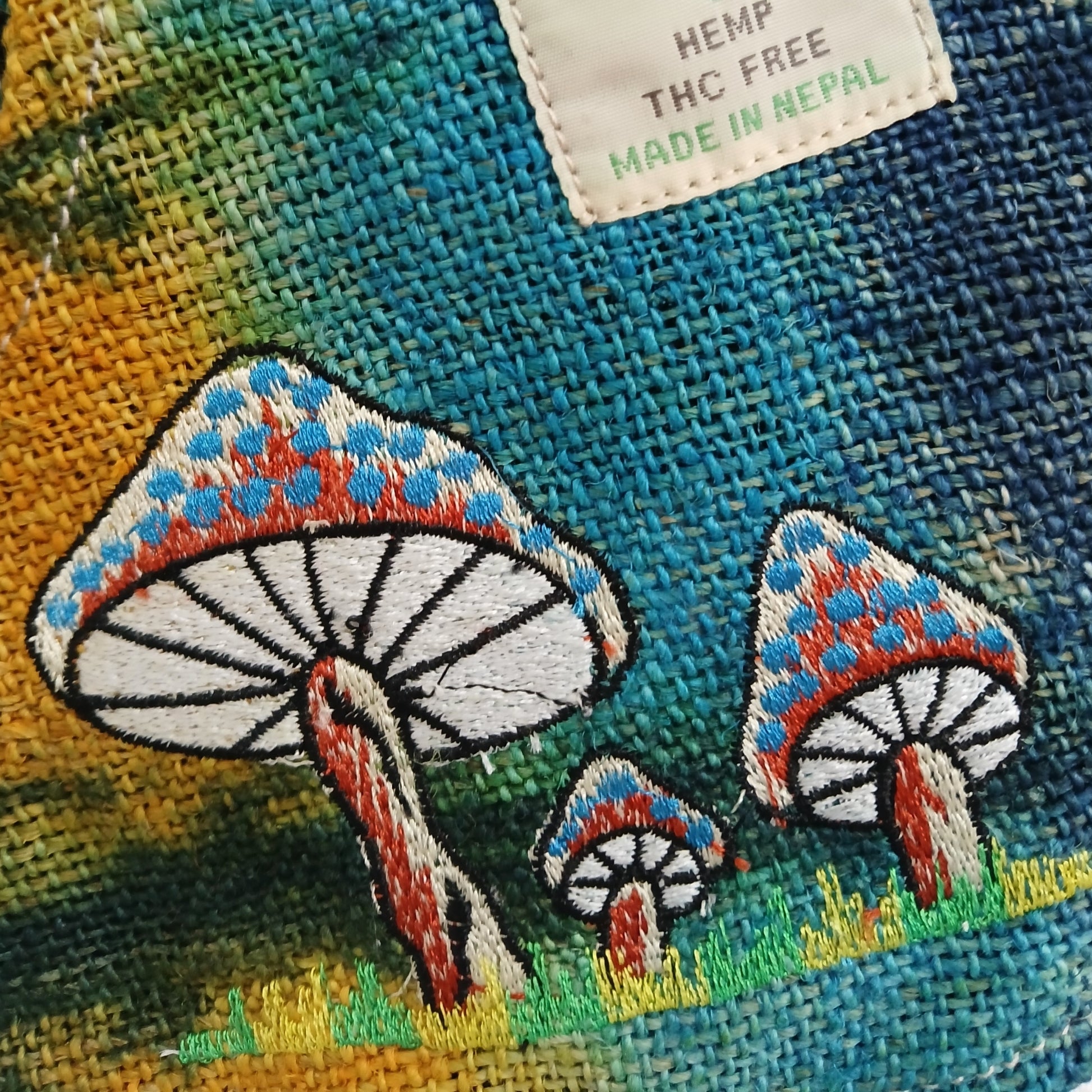 Embroidered mushrooms on a fabric background with a label indicating 'Hemp, THC Free, Made in Nepal'.
