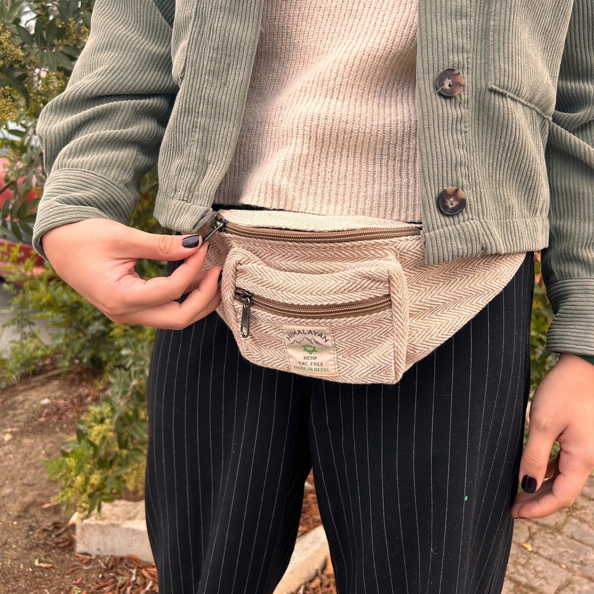 Person wearing a beige fanny pack with a visible brand logo, standing outdoors.