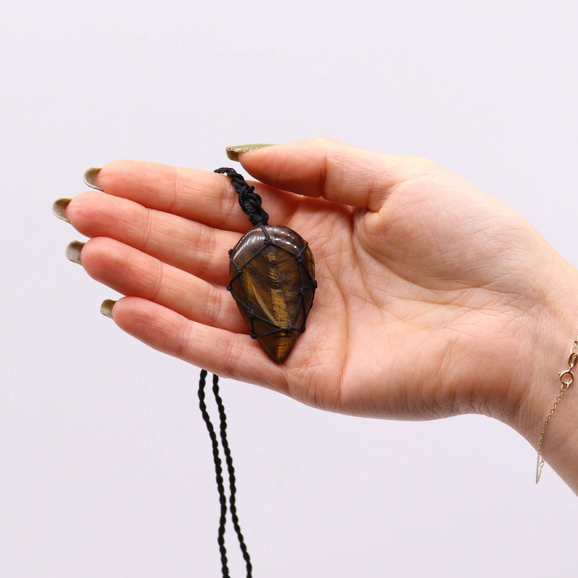 Hand holding a tiger's eye tear drop crystal necklace against a plain background