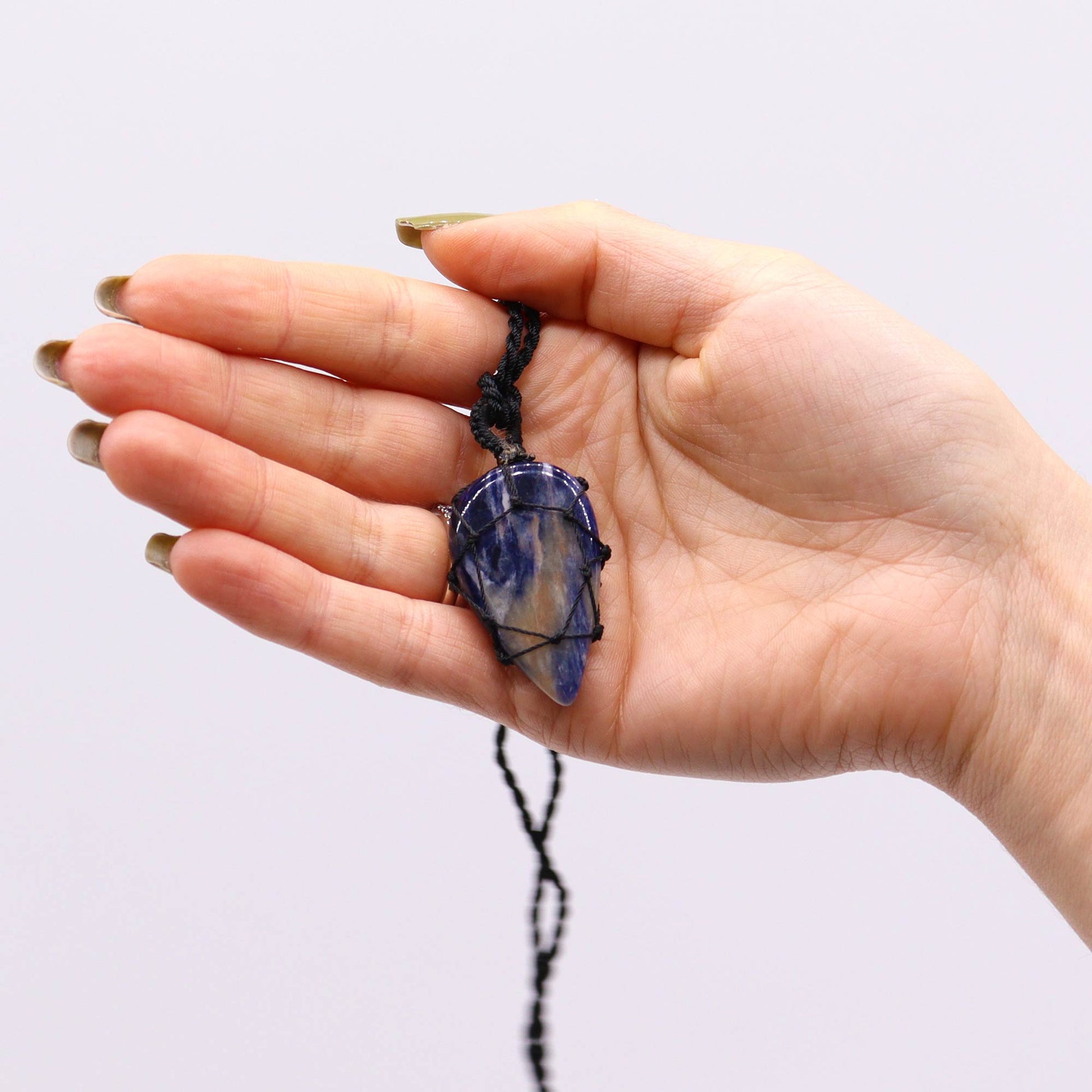 Hand holding a Laced Gemstone Teardrop Pendant - Sodalite with a purple stone against a white background
