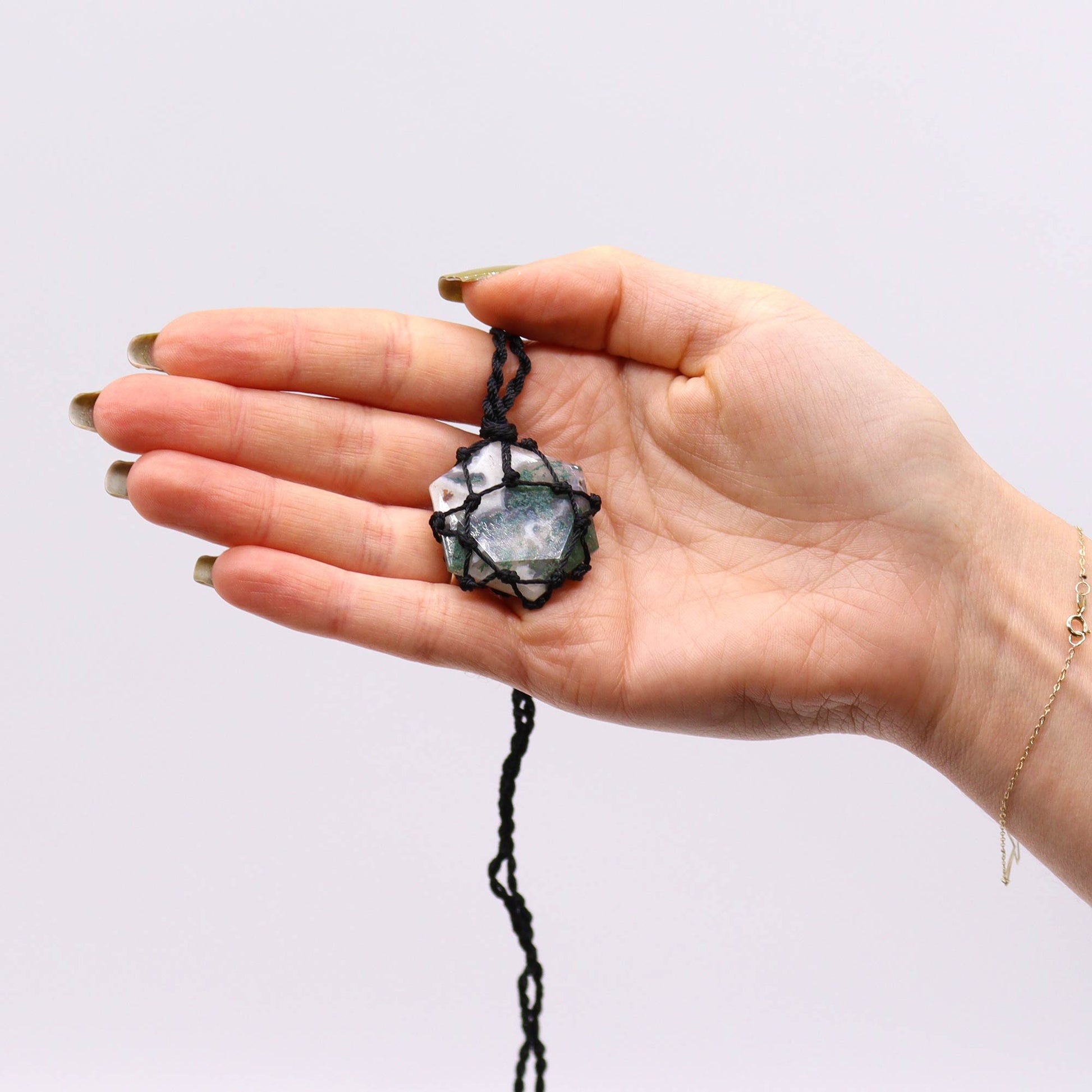Hand holding a Laced Gemstone Hexagon Pendant - Moss Agatea gainst a plain background