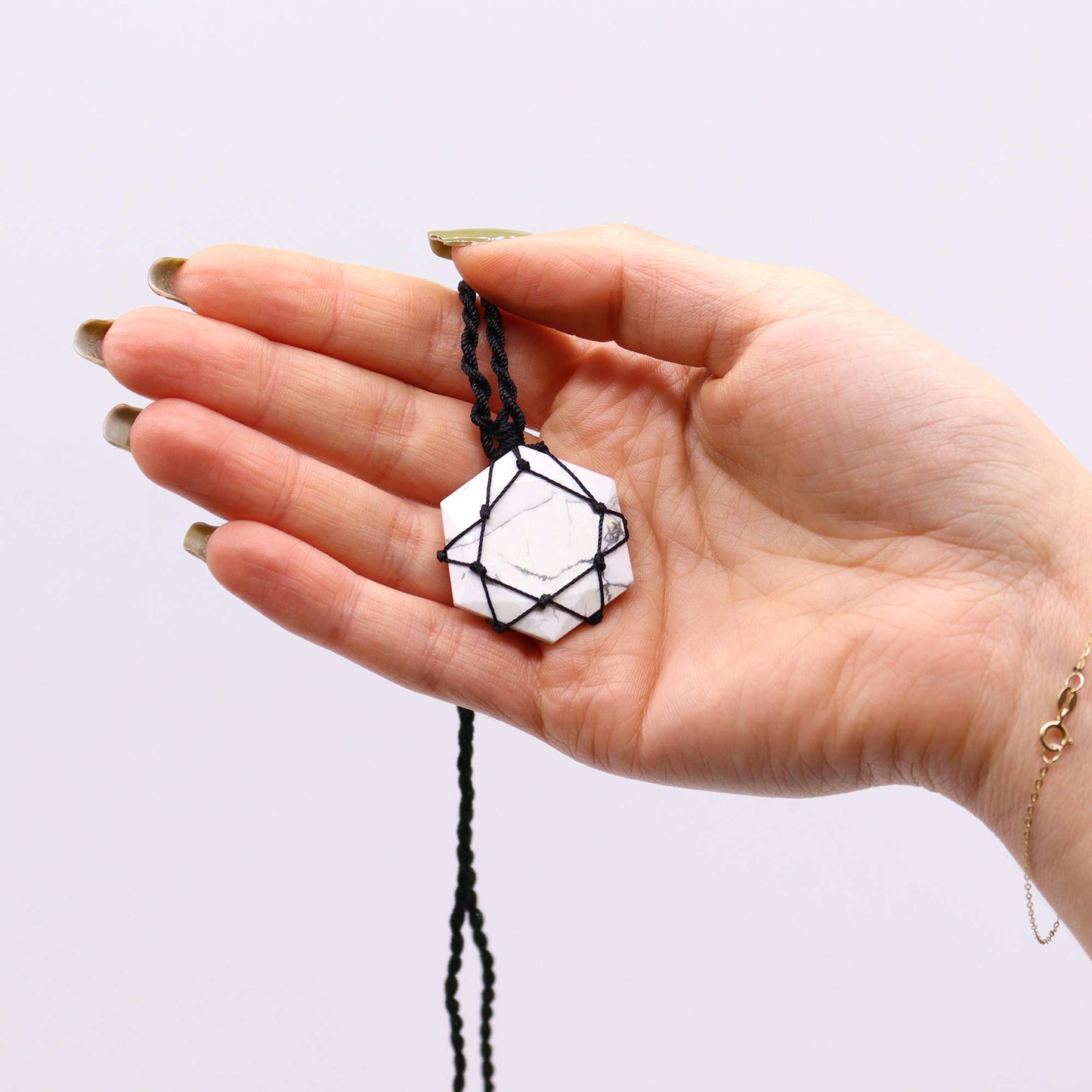 Hand holding a Laced Gemstone Hexagon Pendant - White Howlitewith a white pendant against a light background