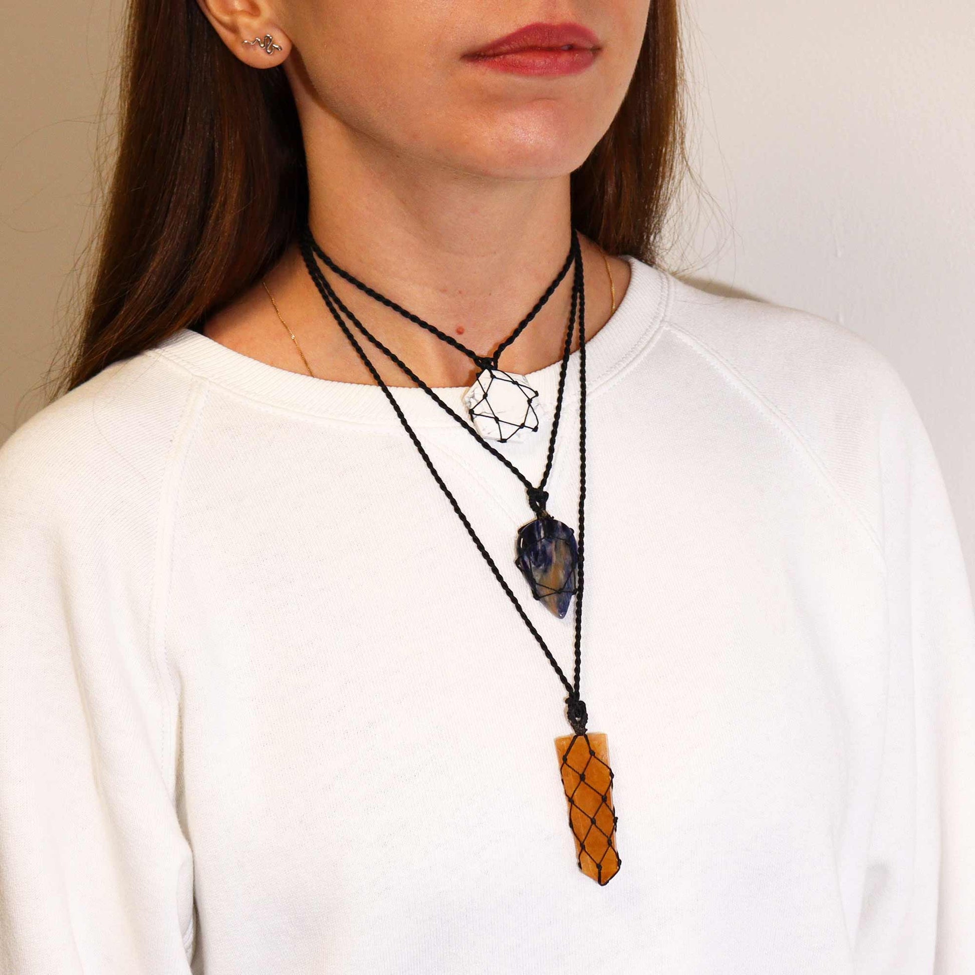 Woman wearing a necklace with multiple pendants an Amethyst  tear drop and golden quartz flat point gainst a neutral background